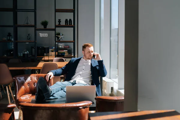 Serious young businessman wearing fashion suit is talking on mobile phone in modern office room