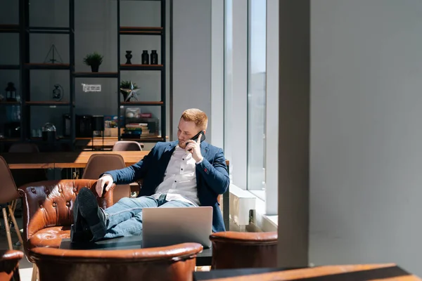 Thinking young businessman wearing fashion suit is talking on mobile phone in modern office room