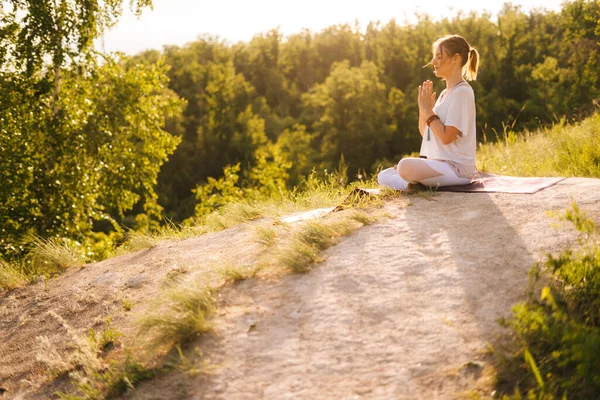 Side view of young woman meditating in lotus position with closed eyes sitting on yoga mat.