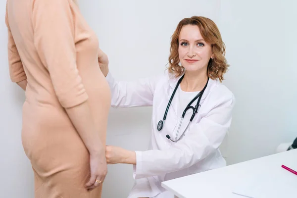 Smiling doctor wearing white coat measure belly waist size of unrecognizable pregnant young woman