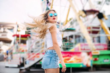 Güzel model kız gülümsüyor ve geri görünüyor dinamik olarak genç kız Genç sokakta yürüyor. Rüzgarda çırpınan saç. Kısa denim şort ve beyaz tişört giyen şık mutlu genç kadın. brightred dudakları