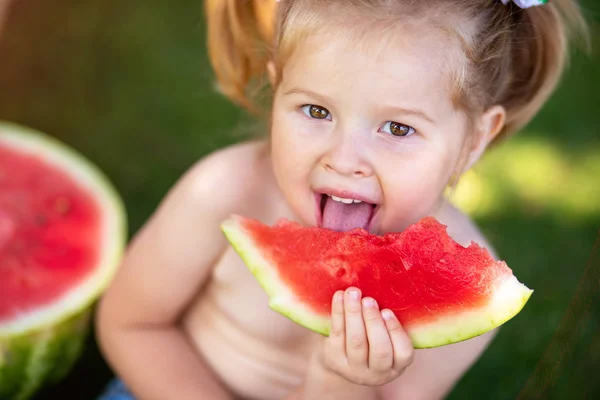 Child eating watermelon in the garden. Kids eat fruit outdoors. Healthy snack for children. Little girl playing in the garden holding a slice of water melon