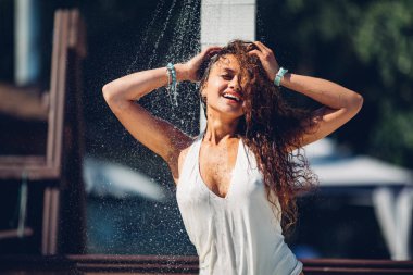 Isı ve ferahlatıcı konsept. Çekici kadının üzerine su damlaları düşüyor. Kumsalda duş alan güzel esmer kız bikinili seksi bayan duş almaktan hoşlanıyor..