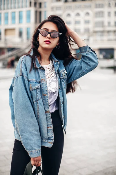 Mujer glamorosa interesada en chaqueta de mezclilla de gran tamaño hace selfi. Hermosa chica morena posando en el fondo de la ciudad —  Fotos de Stock