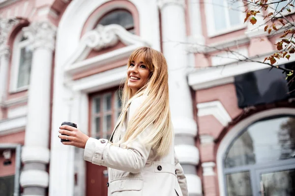 Porträt eines lächelnden Mädchens. Junge glückliche Frau dreht sich und lächelt. Bekleidet mit beigem Trenchcoat. Kaffee to go — Stockfoto