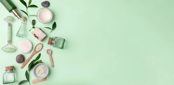 Green spa. massager, facial oil, handmade soap,face cream, mask, body lotion, bath salt.body and face care tools and accessories on light green background, top view.space for text.