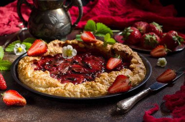 Mayasız hamur çilek pasta için yuvarlak bir şekil ile pasta. Koyu arka plan. Yeşil çilek yaprakları, taze çilek çilek. Kırmızı koşucu. Kırmızı pasta kabuk. Seçici odak. Karanlık fotoğraf.