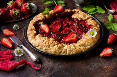 Mayasız hamur çilek pasta için yuvarlak bir şekil ile pasta. Koyu arka plan. Yeşil çilek yaprakları, taze çilek çilek. Kırmızı koşucu. Kırmızı pasta kabuk. Seçici odak. Karanlık fotoğraf.