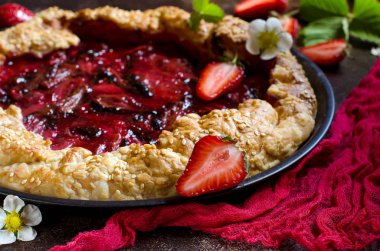 Karanlık bir arka plan üzerinde çilek ile tart. Yeşil çilek yaprakları, taze çilek çilek. Kırmızı koşucu. Kırmızı pasta kabuk. Seçici odak. Karanlık fotoğraf.