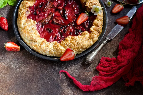 Karanlık bir arka plan üzerinde çilek ile tart. Yeşil çilek yaprakları, taze çilek çilek. Kırmızı koşucu. Kırmızı pasta kabuk. Seçici odak. Karanlık fotoğraf.