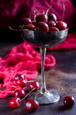 Olgun taze kiraz masanın üzerine güzel bir vazoda kapatın. Çilek su damlaları. Dağınık kiraz masanın üzerinde. Vintage tarzı fotoğrafta. Seçici odak.