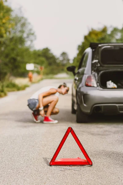 若くてきれいな女性用道路の側に後部タイヤ 問題と他の道路使用者に警告する赤色の三角形が付いている車 — ストック写真
