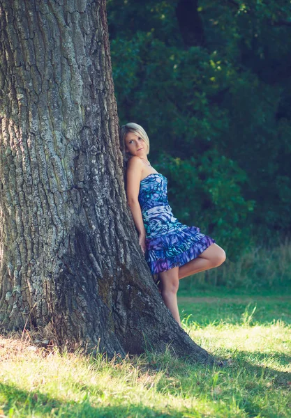 庭の木にもたれるとファッショナブルな若い官能的な金髪女の肖像 — ストック写真