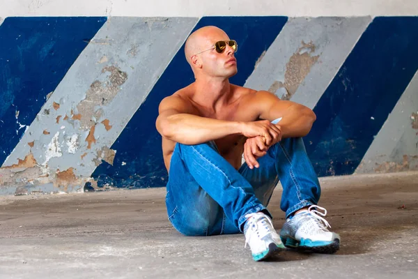 Beautiful male with blue eyes and sexy muscular body wear denim jeans and gold sunglasses with naked torso. Fitness male with healthy tan posing.