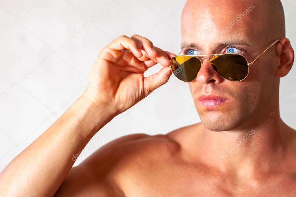 Beautiful male with blue eyes and sexy muscular body wear denim jeans and gold sunglasses with naked torso. Fitness male with healthy tan posing.