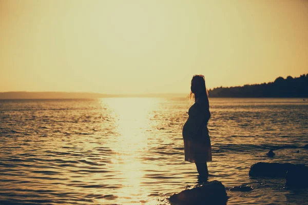 Gün batımında denizde su ile oynayan güzel genç hamile kadın Concept Love ve gebelik