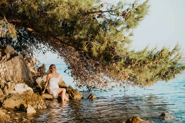 Beyaz ıslak elbise ile güzel genç hamile kadın deniz suyu yakın kayalar üzerinde dinlenmek gün batımı konsept aşk ve hamilelik