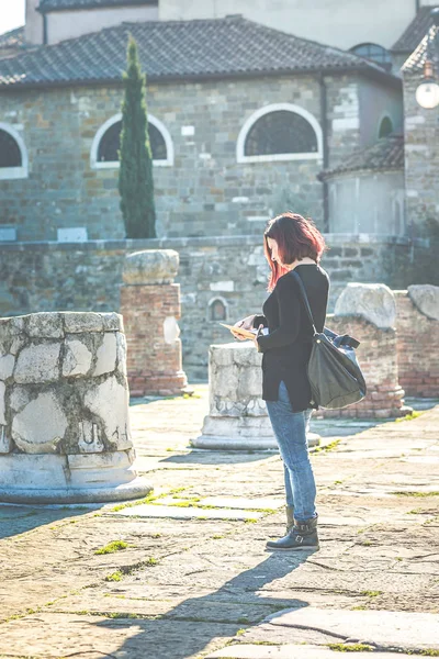 Woman reading book walking in old garden with building ruins