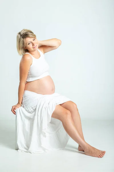 Pregnant woman in white top and skirt posing in studio