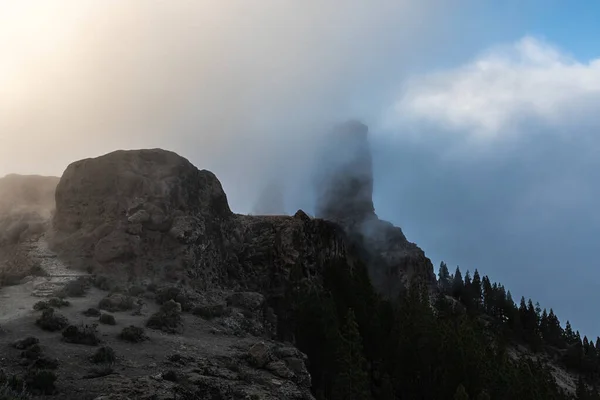 Gün batımında dağların üzerinden bulutların içinde Roque Nublo Kayası 'na giden yol.