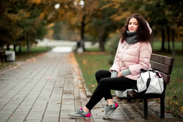 girl in a sports style sits on a bench in the park