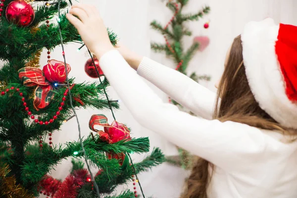 Ένα κορίτσι σε ένα καπέλο santa στολίζει ένα χριστουγεννιάτικο δέντρο — Φωτογραφία Αρχείου