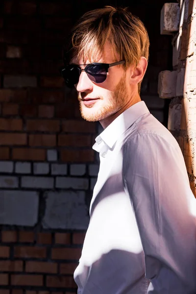 bir tuğla duvar önünde güneş gözlüğü moda adam