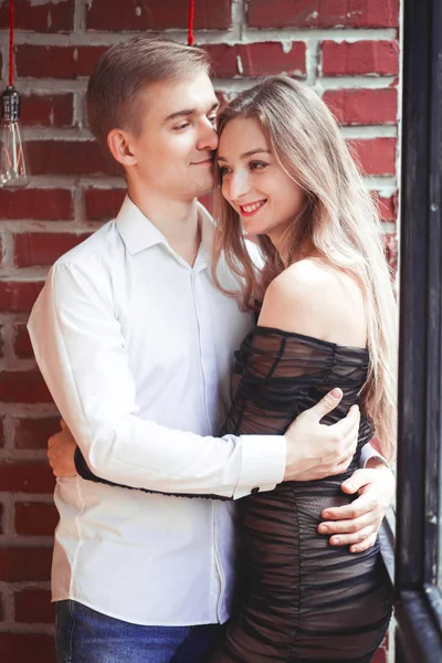 Ung man och kvinna som kramas mot en tegelvägg — Stockfoto