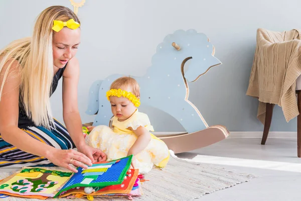 Mamá y su hija están sentadas en el suelo y mirando un libro de fieltro . — Foto de Stock