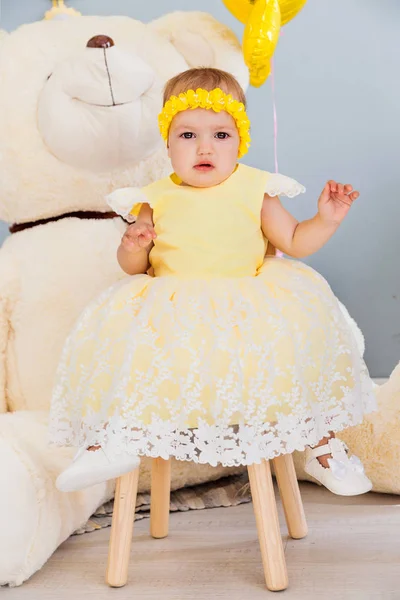 Una niña está sentada en una silla con un vestido amarillo . —  Fotos de Stock