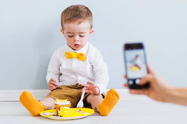 Mom takes a photo or video on the phone as her son eats cake