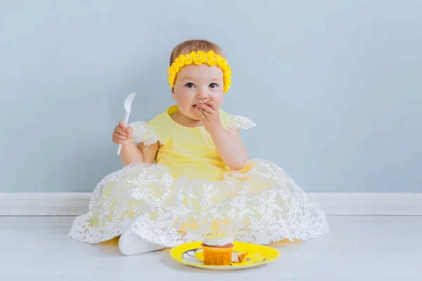 Menina em vestido amarelo come bolo sentado no chão — Fotografia de Stock