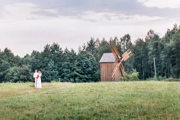 Νύφη και γαμπρός ποζάρουν με φόντο ένα παλιό ξύλινο μύλο — Φωτογραφία Αρχείου