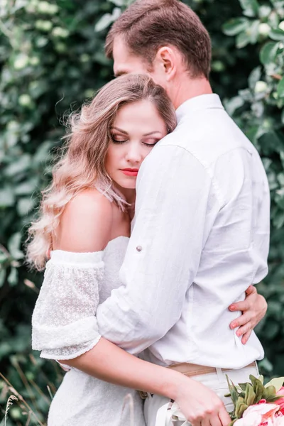 Noiva e noivo com um buquê de peônias posando no pano de fundo da floresta — Fotografia de Stock