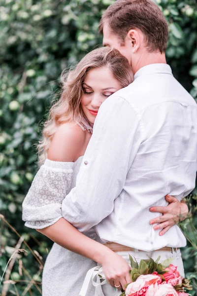 Bride and groom with a bouquet of peonies posing against the backdrop of the forest — Stock Photo, Image