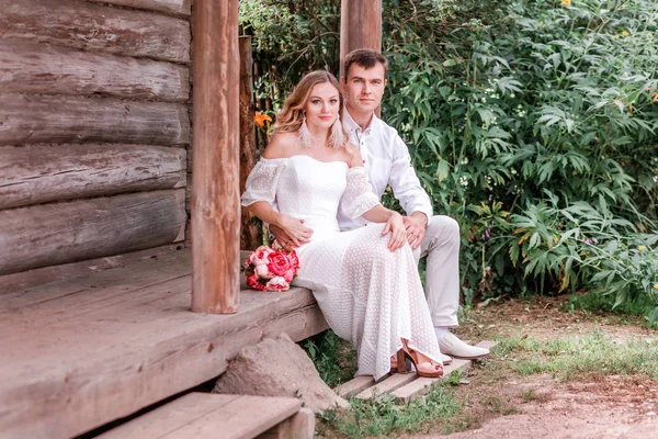 Bride and groom are sitting on the threshold of a wooden house — Stock Photo, Image