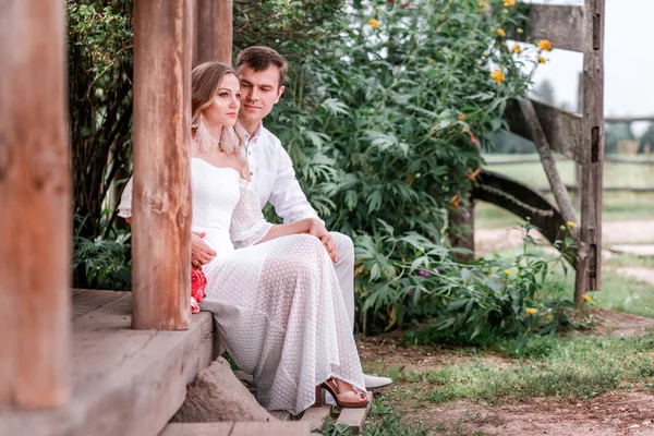 Bride and groom are sitting on the threshold of a wooden house — Stock Photo, Image