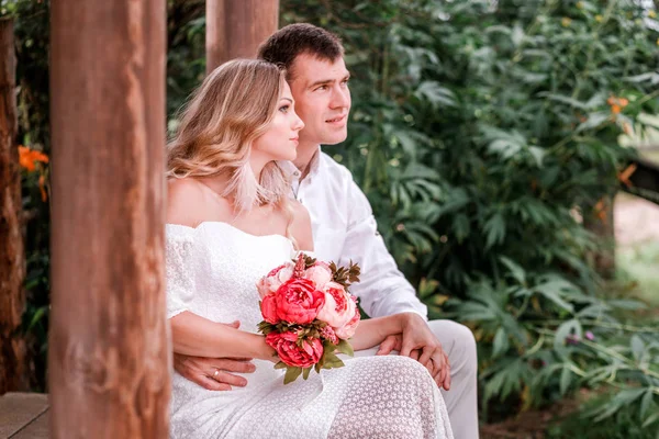 Bride and groom are sitting on the threshold of a wooden house — Stock Photo, Image