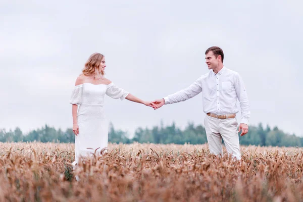 Νύφη και γαμπρός, κρατώντας τα χέρια στο φόντο ενός πεδίου σιτάρι — Φωτογραφία Αρχείου