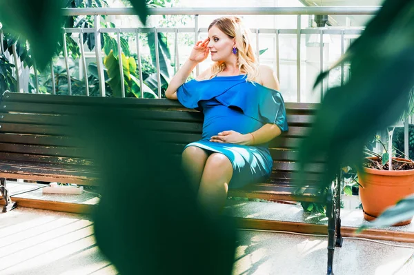 Gelukkige zwangere vrouw zittend op een bankje in de botanische tuin — Stockfoto