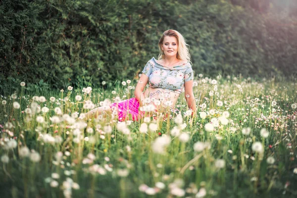 Pregnant woman with mehendi pattern on her belly is sitting on the field with dandelions — Stock Photo, Image