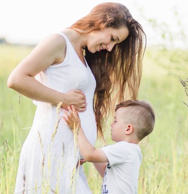 Oğlu ile çayırda beyaz elbiseli güzel hamile kadın