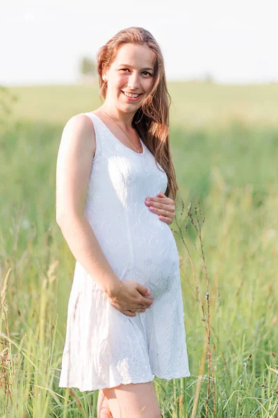 Красивая беременная женщина в белом платье на лугу — стоковое фото
