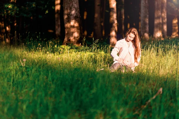 一个孕妇坐在森林的边缘，在傍晚的阳光下. — 图库照片