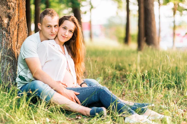 Gravid kvinna och hennes man sitter på gräset — Stockfoto
