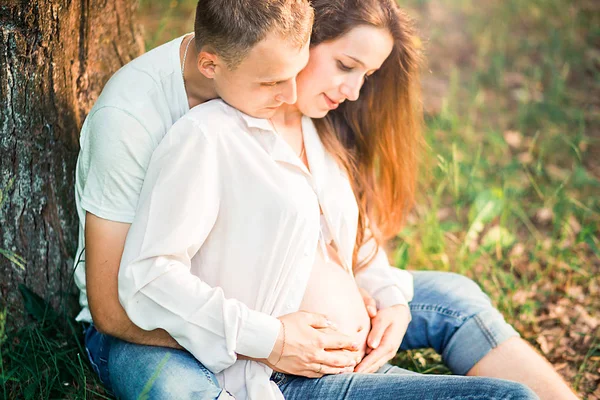 Kobieta w ciąży i jej mąż siedzą na trawie — Zdjęcie stockowe