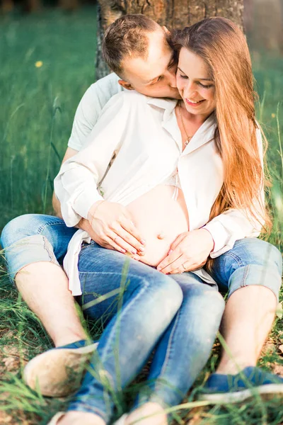 Zwangere vrouw en haar man zitten op het gras — Stockfoto