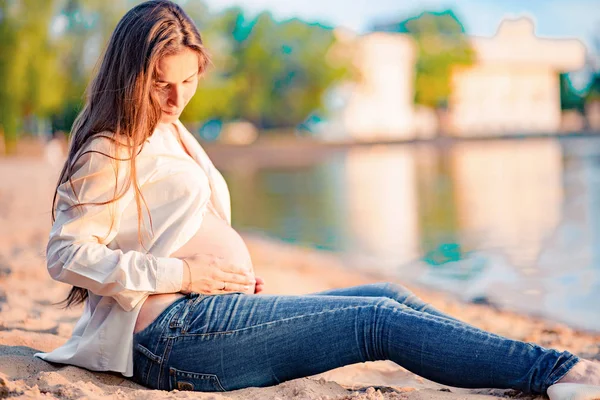 美丽的孕妇坐在河边的日落 — 图库照片