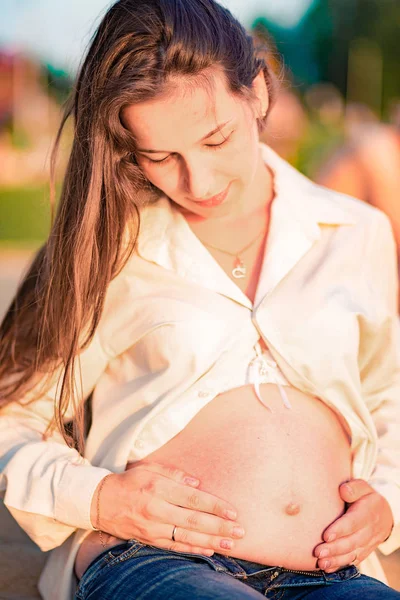 Hermosa mujer embarazada sentada junto al río al atardecer —  Fotos de Stock
