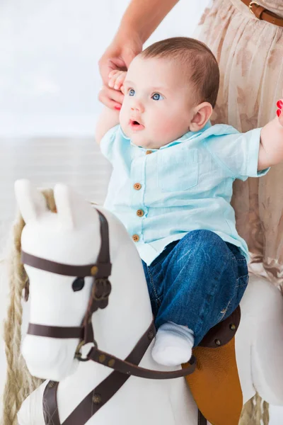 Una madre feliz ayuda a un pequeño hijo a montar un caballo de juguete . —  Fotos de Stock